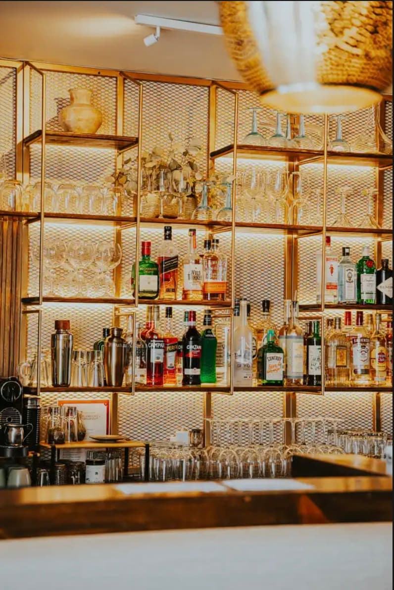 Estantería dorada de la barra con destilados, coctelería y cristalería.
