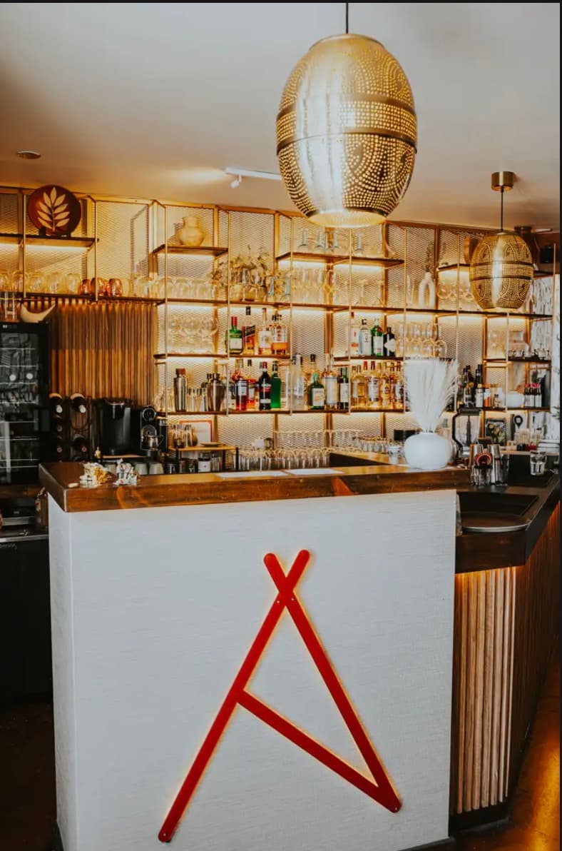 La barra de Aldeano, con el logo en rojo sobre el frente y la estantería dorada retroiluminada detrás.