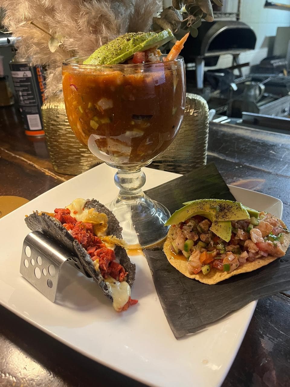 Copa de camarones al estilo Sinaloa con aguacate, taco gratinado y tostada de atún, servidos en la barra.