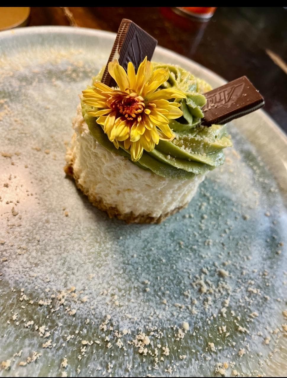 Mini pastel de matcha y queso crema, decorado con una flor comestible y barras de chocolate Andes.